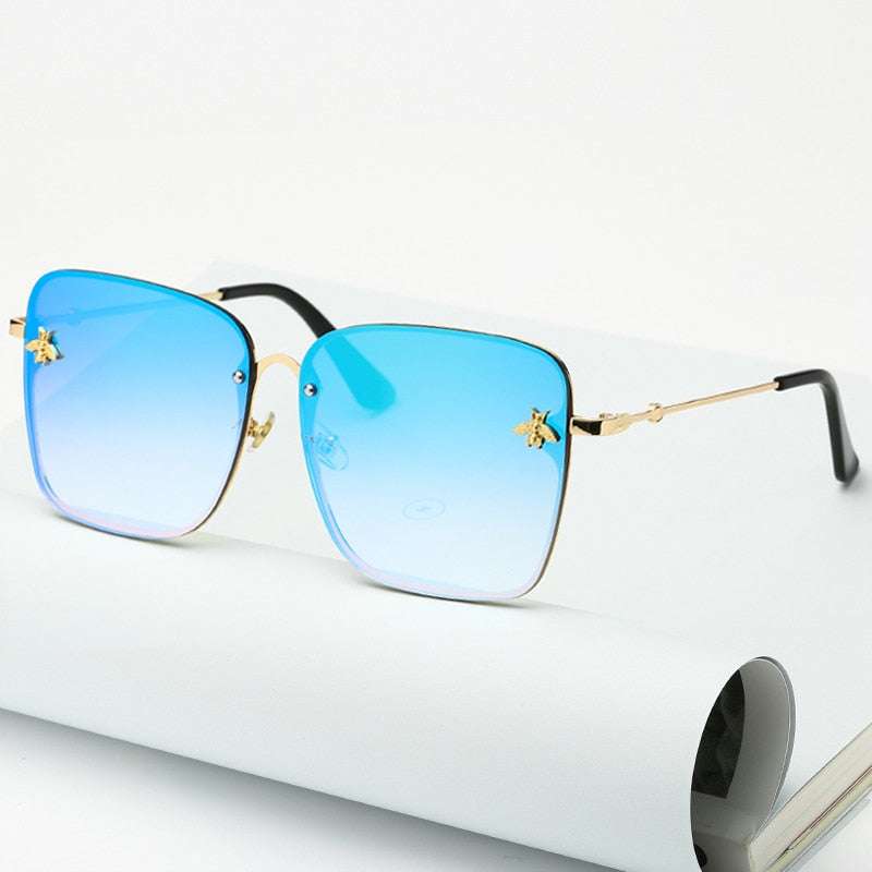 Lunettes de soleil carrées sans monture pour femme avec verres dégradés UV400 et branches dorées, posées sur un carnet blanc. Accessoire tendance mode.