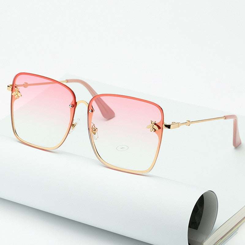 Lunettes de soleil carrées sans monture pour femme avec verres dégradés UV400 et branches dorées, posées sur un carnet blanc. Accessoire tendance mode.