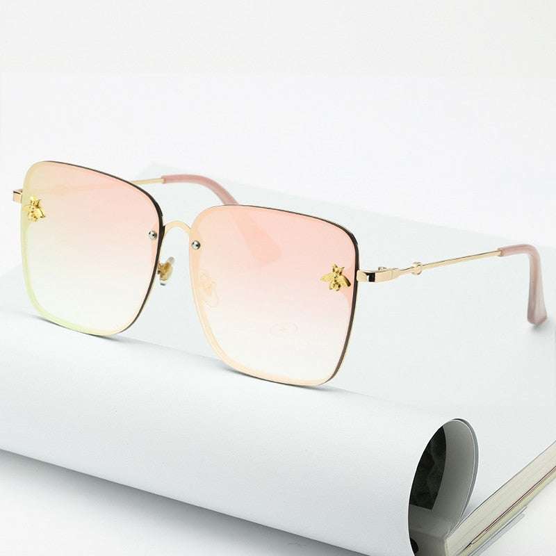 Lunettes de soleil carrées sans monture pour femme avec verres dégradés UV400 et branches dorées, posées sur un carnet blanc. Accessoire tendance mode.