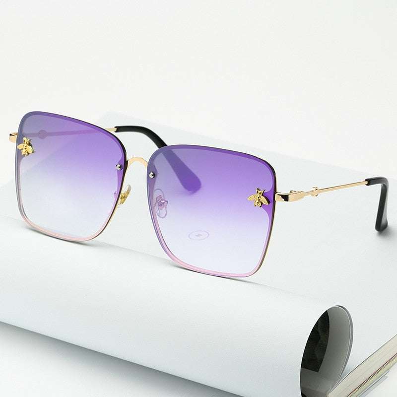 Lunettes de soleil carrées sans monture pour femme avec verres dégradés UV400 et branches dorées, posées sur un carnet blanc. Accessoire tendance mode.